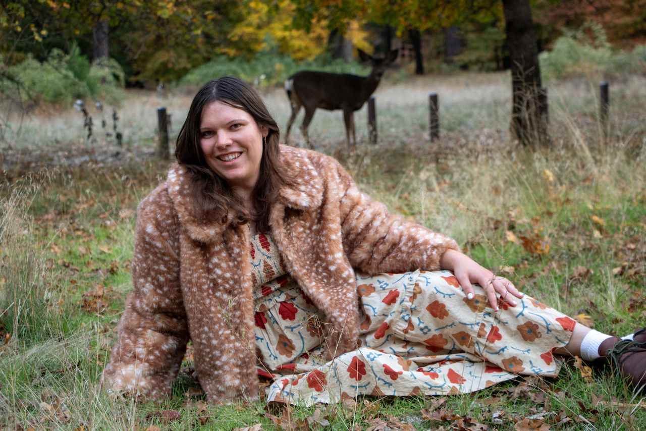 A figure sits as deer walk behind them.