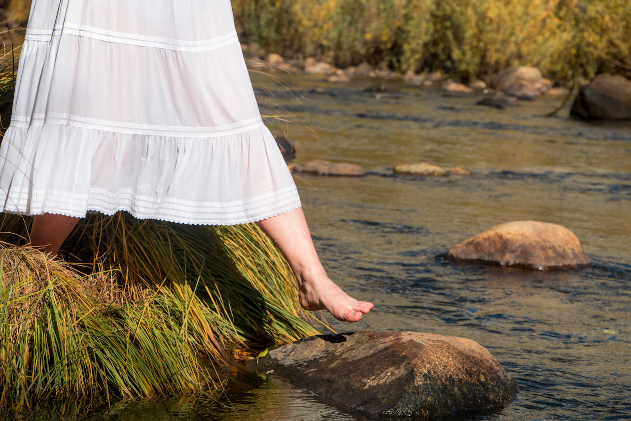 A person steps between rocks in a stream