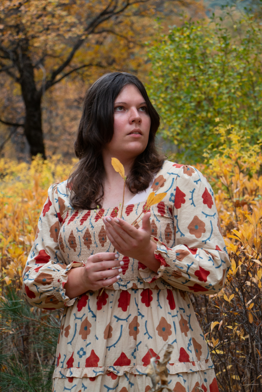 A figure holds a stem amidst a golden forest in autumn.